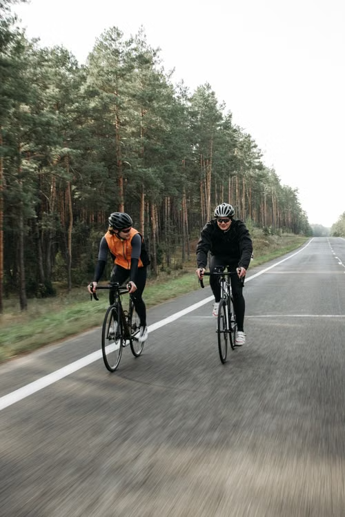 Two recreational cyclists riding side by side and talking on a quiet road bordered by trees