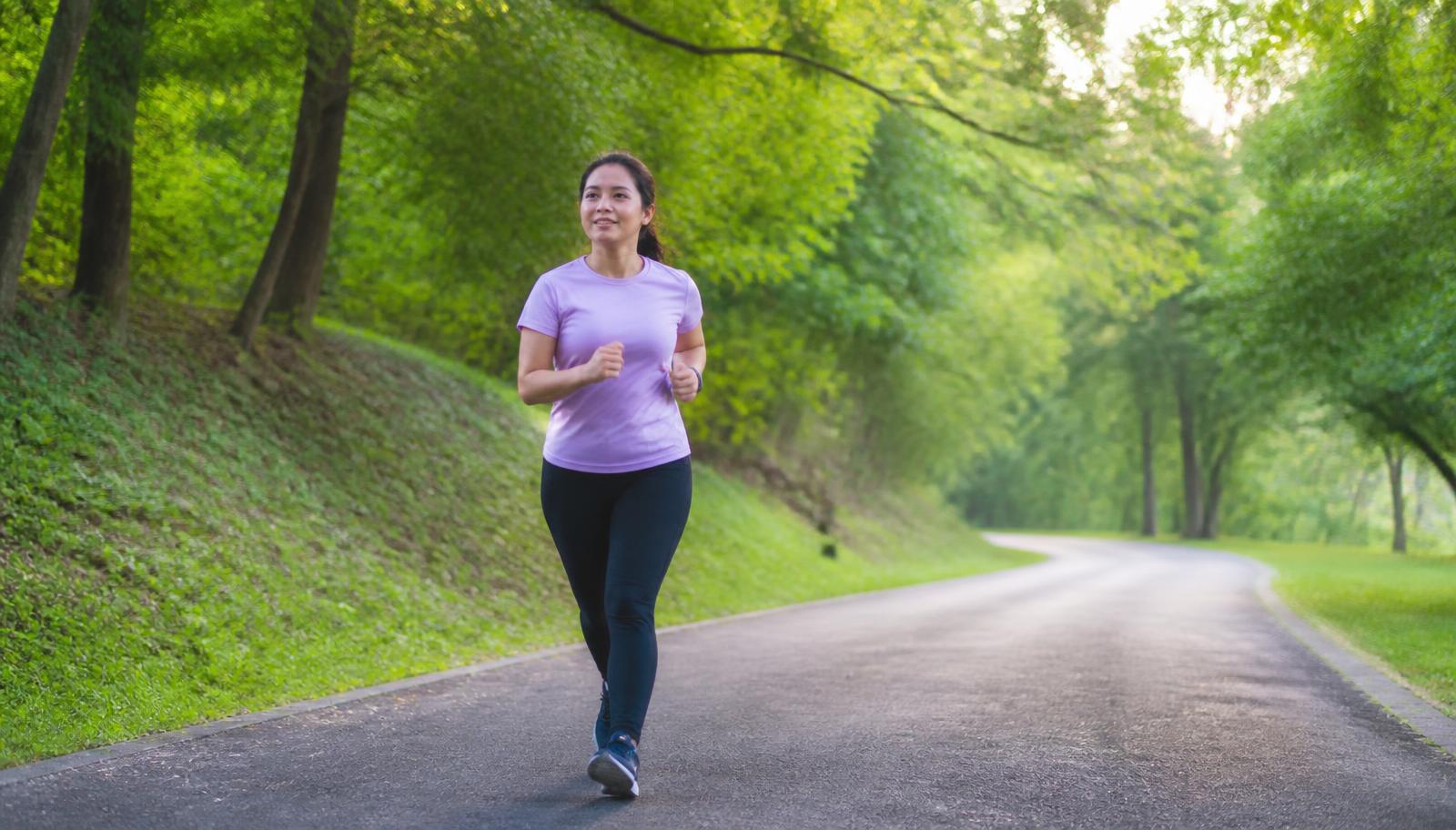 A beginner runner jogging at an easy pace on a wide park path in soft morning light
