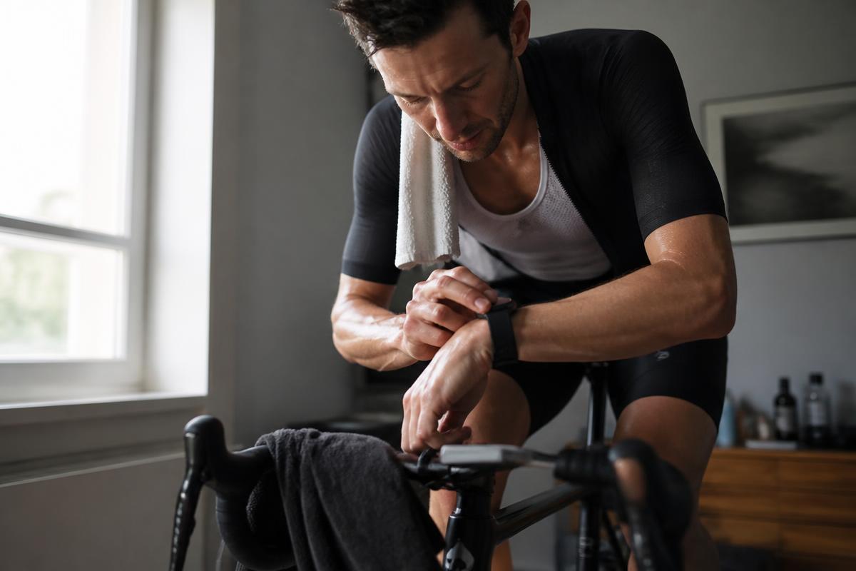 A cyclist checking a smartwatch while training indoors on a turbo trainer
