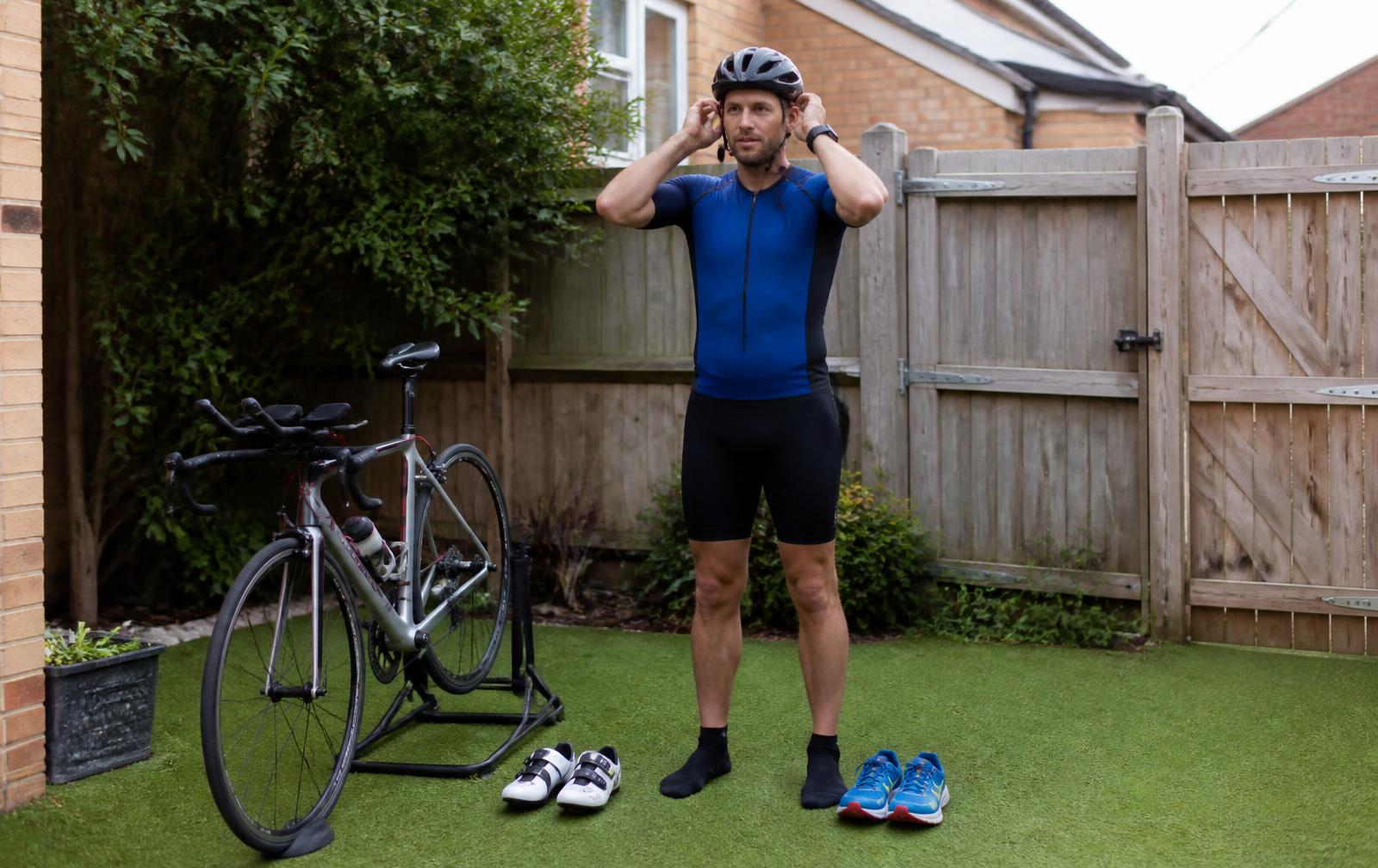 Recreational triathlete practising putting on a cycling helmet beside a bike and two pairs of shoes at home
