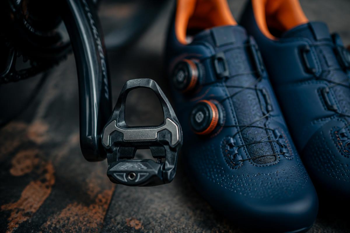 Close-up of a clip-in road bike pedal next to a pair of navy cycling shoes
