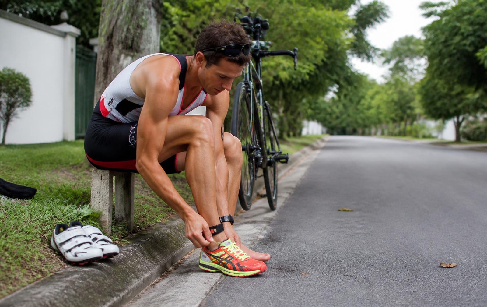 Triathlete swapping cycling shoes for running shoes beside their bike before a short brick run